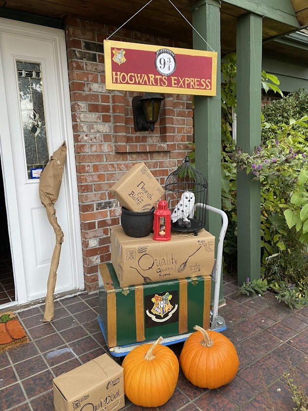 Platform 9 ¾ entrance setup with a Hogwarts Express sign for a Harry Potter party with a trolley, wrapped parcels, an owl in a cage, pumpkins, and a lantern.