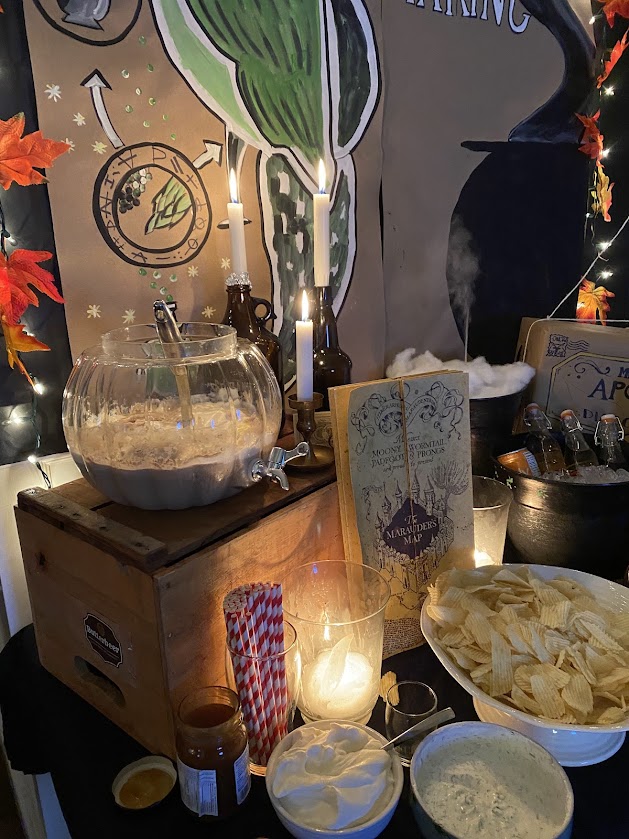 Harry Potter party bar set up with a pumpkin glass dispenser in the potions classroom with candlesticks, cauldrons, potions, Marauders map, painted Harry Potter symbols