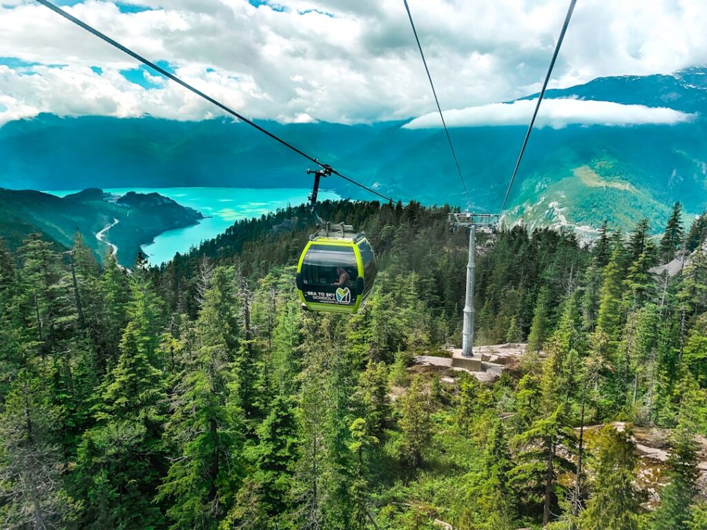 green and black cable car over green pine trees under blue sky during daytime sea to sky gondola squamish British Columbia Canada