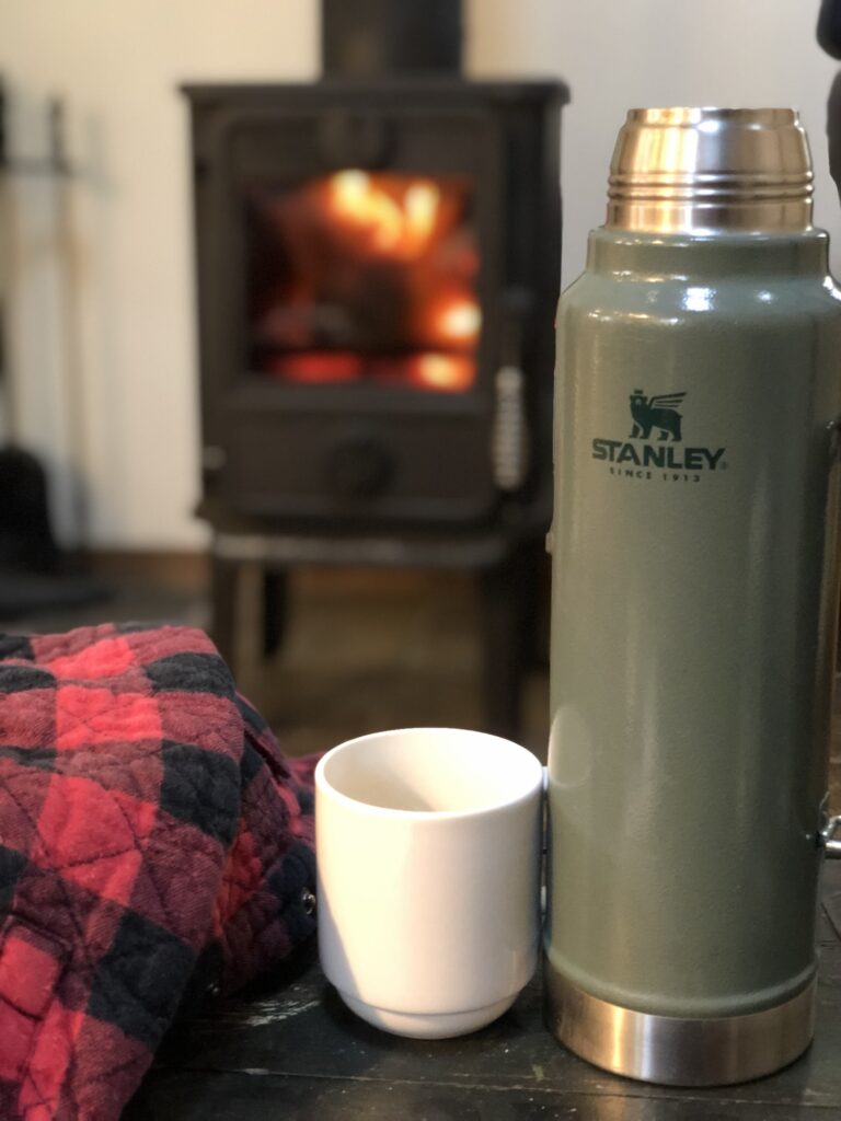 Stanley thermos with a white mug in front of wood burning fire place